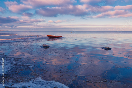 Stunning winter sunset on the frozen Peipsi lake near the fishers Nina village in Estonia, the old boat in the water