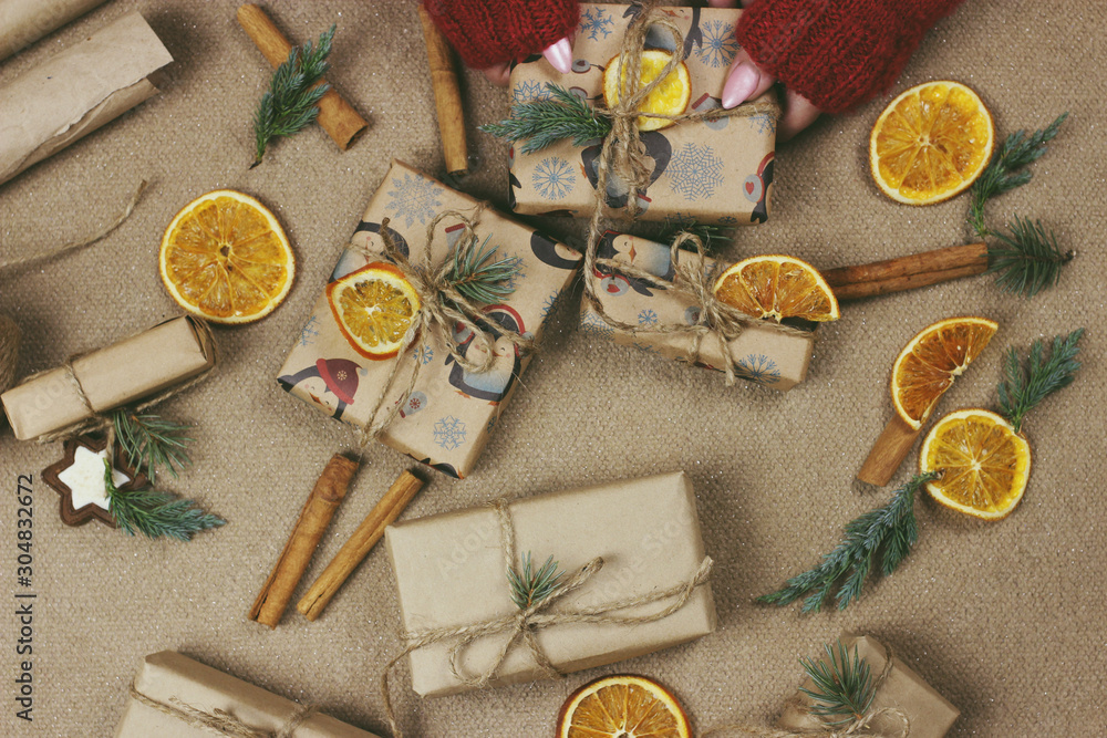 Fototapeta premium A woman wraps Christmas presents in wrapping paper and ties a ribbon bow. Close-up of woman's hands preparing surprises for the new year. Workflow of a derator. Desktop.