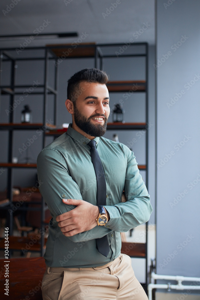 Smiling happy middle eastern businessman or leader standing in office and look side. successful team leader wearing formal wear shirt and tie, posing for photo at workplace Smiling happy middle eastern businessman or leader standing in office and look side. successful team leader wearing formal wear shirt and tie, posing for photo at workplace