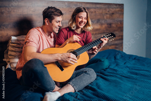 boyfriend and girlfriend playing the guitar, young caucasian couple in love with each other in bedroom.