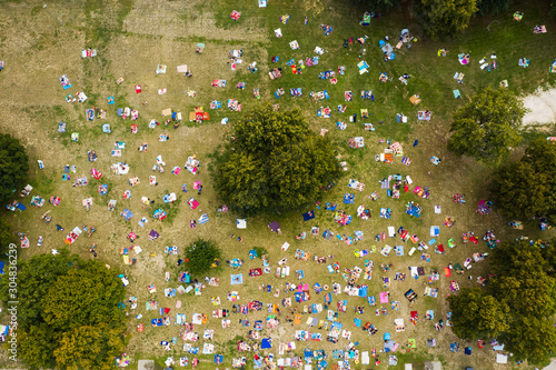 Top view of a crowd of people resting on the grass in a water park. People sunbathe and relax on rugs and wards on green grass.