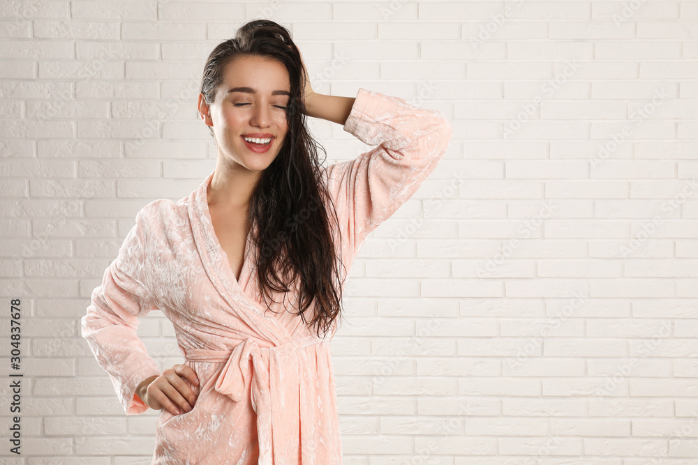 Young woman in bathrobe with wet hair near white brick wall. Space for text Young woman in bathrobe with wet hair near white brick wall. Space for text