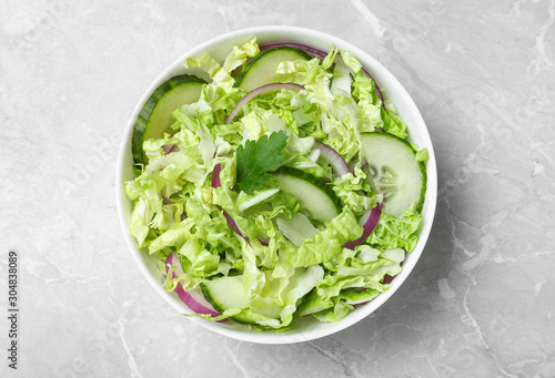 Tasty salad with cabbage and cucumbers on light grey marble table  top view