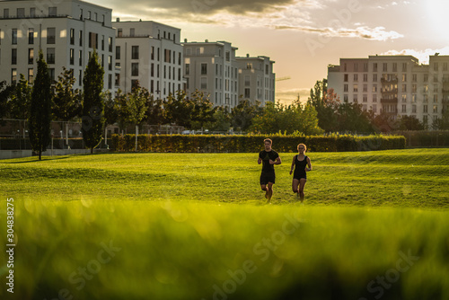Two young attractive athletes run in the park of a modern city