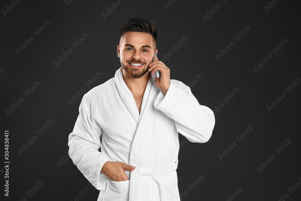 Young man in bathrobe talking on mobile phone against black background Young man in bathrobe talking on mobile phone against black background