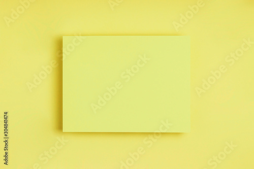Minimal frame geometric composition mock up. Blank sheet of paper postcard on delicate yellow background. Template design invitation card. Top view, flat lay, copy space. Horizontal orientation.
