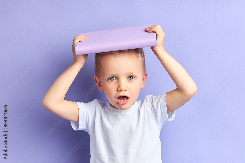 Caucasian little boy tired of reading book, hold book above head. Kid's expressions of upset and fatigue