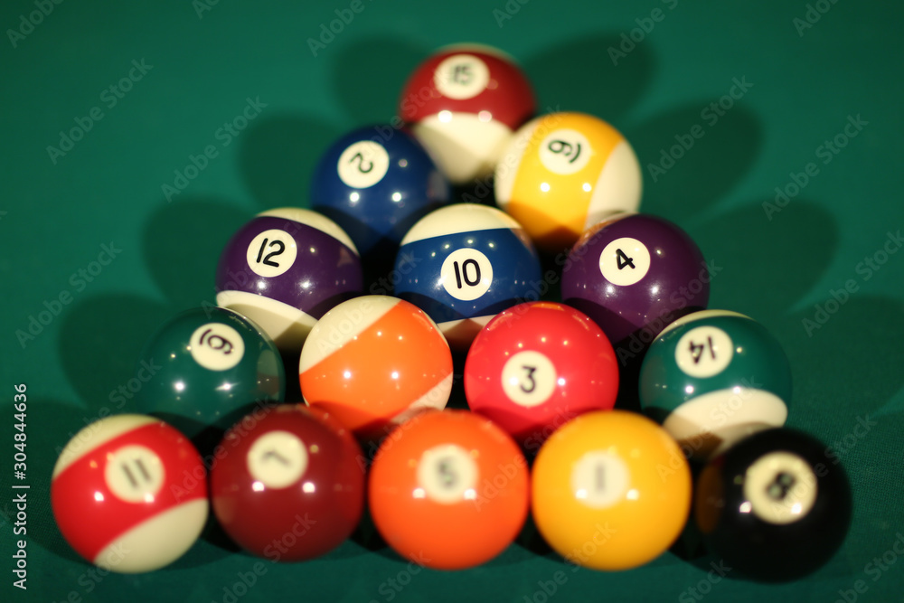 Sports game of billiards on a green cloth. Multi-colored billiard balls in the shape of a triangle with numbers on the pool table. Active leisure and entertainment. Billiards billiard balls close up. Sports game of billiards on a green cloth. Multi-colored billiard balls in the shape of a triangle with numbers on the pool table. Active leisure and entertainment. Billiards billiard balls close up.