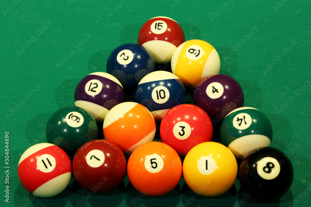 Sports game of billiards on a green cloth. Multi-colored billiard balls in the shape of a triangle with numbers on the pool table. Active leisure and entertainment. Billiards billiard balls close up. Sports game of billiards on a green cloth. Multi-colored billiard balls in the shape of a triangle with numbers on the pool table. Active leisure and entertainment. Billiards billiard balls close up.