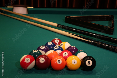 Sports game of billiards on a green cloth. Multi-colored billiard balls in the form of a triangle with numbers, two cues, a cue ball and a triangle on a pool table. Billiards billiard balls close up.