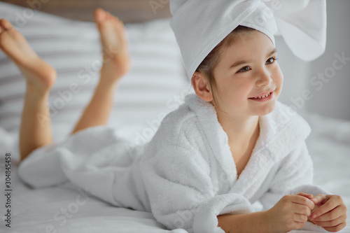 awesome cute little girl of caucasian appearance wearing bathrobe and towel, lies on bed