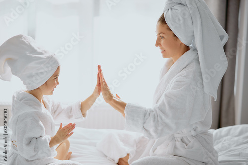 attractive beautiful female clap hands with each other, wearing bathrobe and towel, white bedroom background, white bed