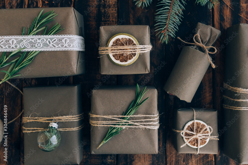 Presents and gifts wrapped in craft paper with decoration on brown wooden background. Holiday zero waste concept.
