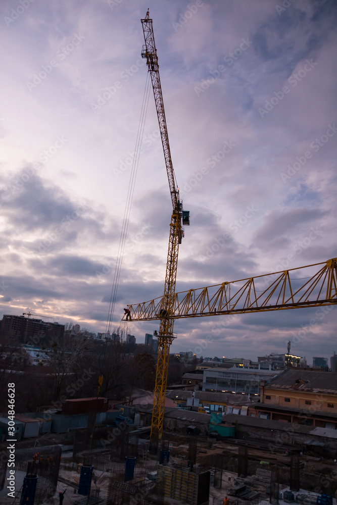 Construction site and cranes in the early evening. Workers on the crane and construction site Construction site and cranes in the early evening. Workers on the crane and construction site