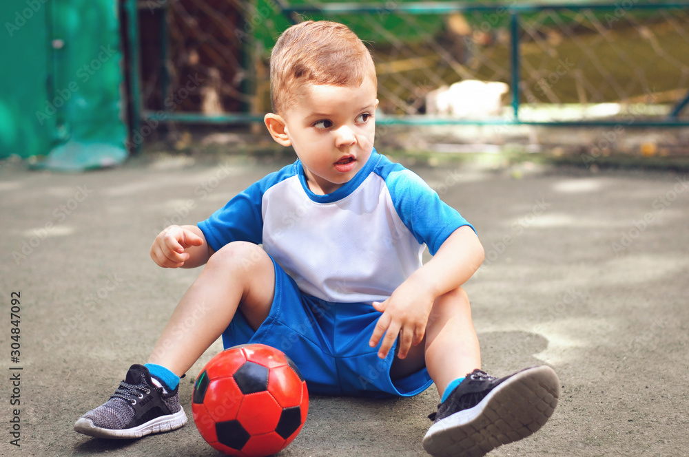 Little three year old boy in blue football uniform and with his red soccer ball Little three year old boy in blue football uniform and with his red soccer ball