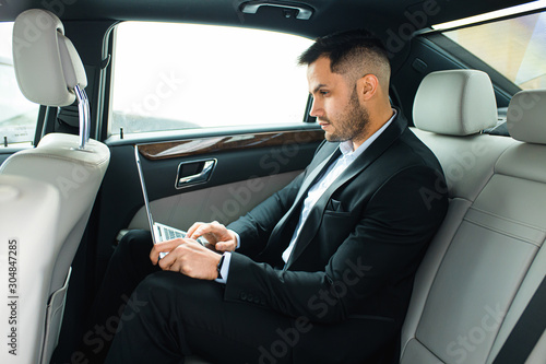 Confident man in tuxedo sit using laptop, working in car, man with beard