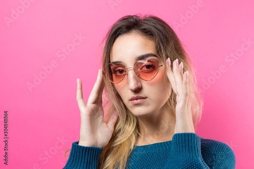 Romantic blonde-haired girl in trendy heart glasses posing with shy smile. Studio close-up portrait © Mountains Hunter