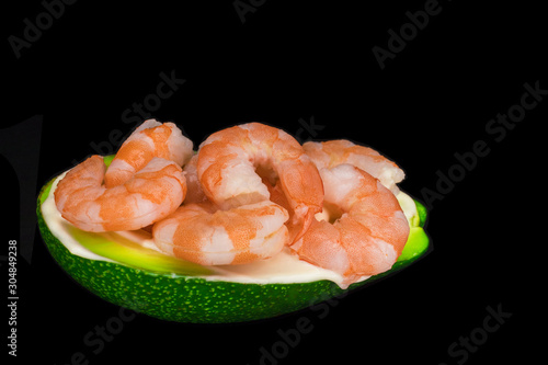 A dish, meal of half fresh avocado and peeled shrimp isolated on black background. Tasty healthy food with vegetables and seafood, low kea.