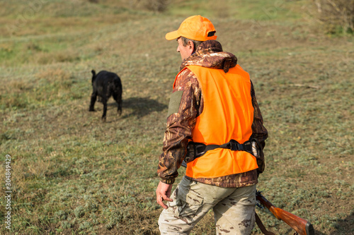 Hunting period, autumn season open. A hunter with a gun in his hands in hunting clothes in the autumn forest in search of a trophy. A man stands with weapons and hunting dogs tracking down the game. 