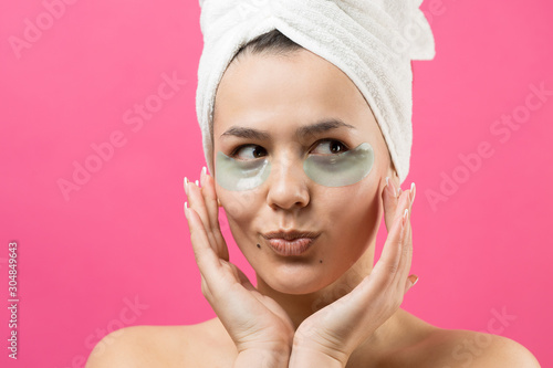 Young beautiful girl in a white towel on his head wears collagen gel patches under her eyes. Mask under eyes treatment face. 