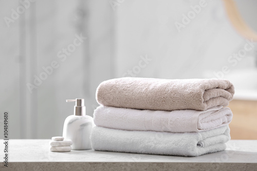 Clean towels, spa stones and soap dispenser on table in bathroom
