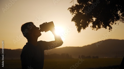 silhouette of fit young man drinking water with sun behind it in sunset