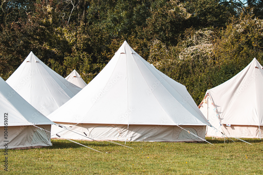 Light creme canvas waterproof tent in a green field on a nice and hot summer day. Blue Clouds, green grass, Child festival tent.