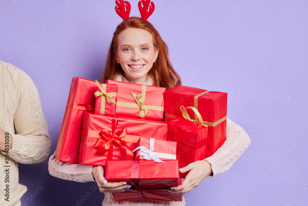Smiling playful girl happily carrying many beautiful Christmas present, finding lots of presents under Christmas tree, wearing funny red horns, looking at camera with cheerful face, happy celebration Smiling playful girl happily carrying many beautiful Christmas present, finding lots of presents under Christmas tree, wearing funny red horns, looking at camera with cheerful face, happy celebration