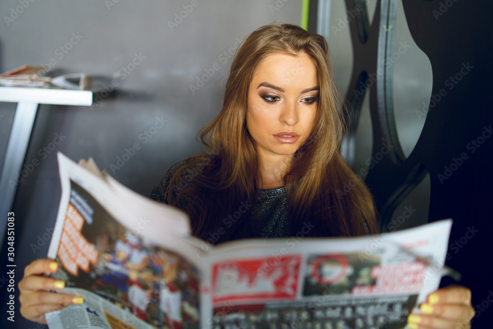 Fototapeta premium Young girl woman sitting at the cafe or restaurant or at home holding and reading newspapers reacting to the article news making faces