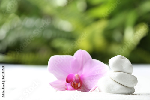 Stack of white stones and beautiful flower on sand against blurred green background. Zen, meditation, harmony