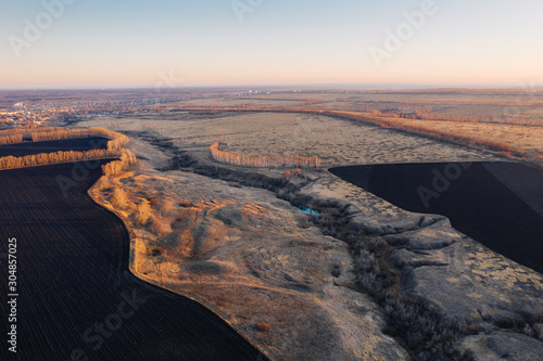 Ravine among agricultural fields in late autumn at sunset, aerial view. Land erosion and agriculture. Rural landscape in cold off-season