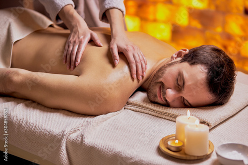 Young caucasian man relax during massage on back made by female hands, lying on spa table, enjoy spa treatment