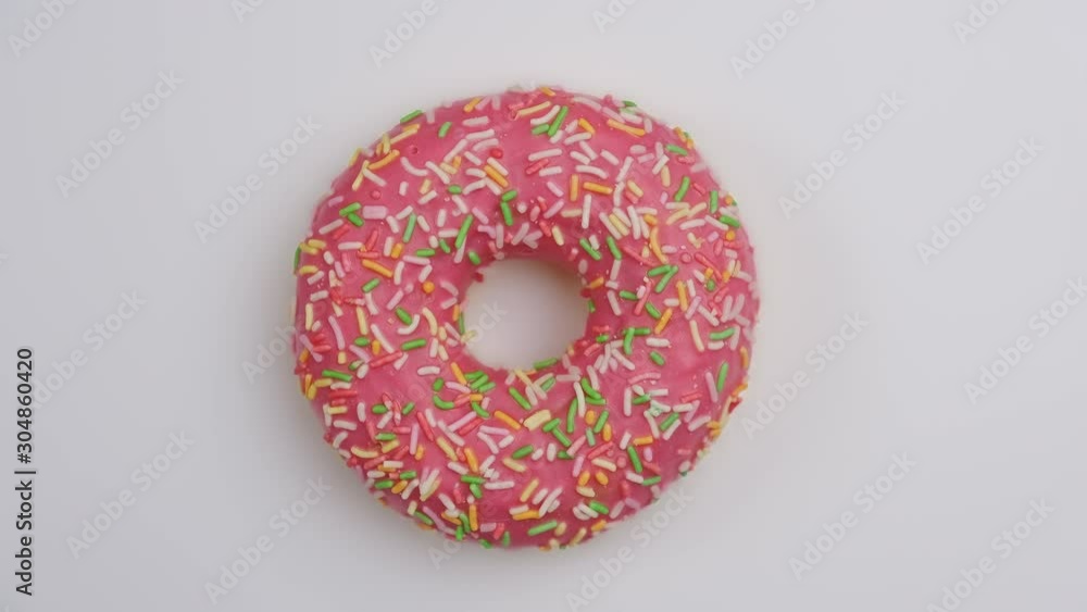 Delicious pink donut with colorful sprinkles rotating at white background. Top view of colorful doughnut spinning. Food concept. Close-up in 4K, UHD Delicious pink donut with colorful sprinkles rotating at white background. Top view of colorful doughnut spinning. Food concept. Close-up in 4K, UHD