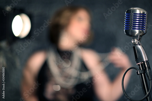 Girl singing in a retro microphone. Recording a clip in the studio of a professional singer. Close up face of singer with microphone on smoky gray background. The singer sings a song on stage.