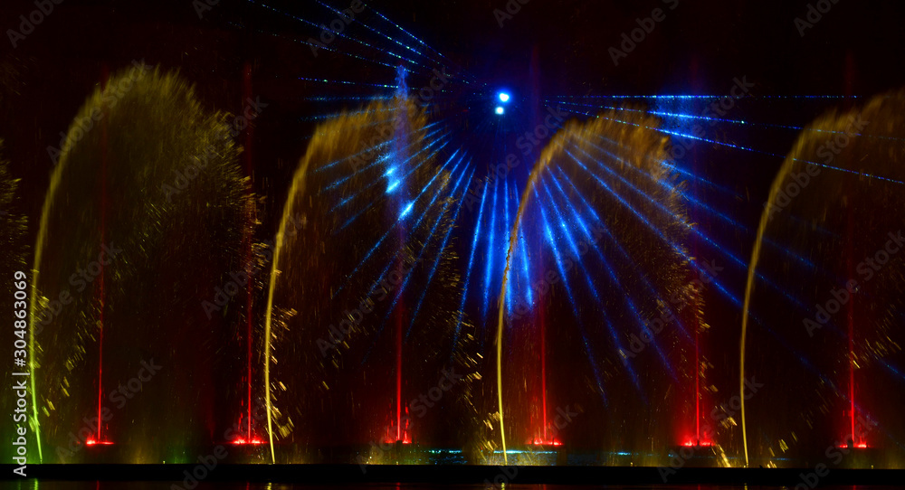 Colorful water fountains. Beautiful laser and fountains show. Large multi colored decorative dancing water jet led light fountain show at night. Dark background.