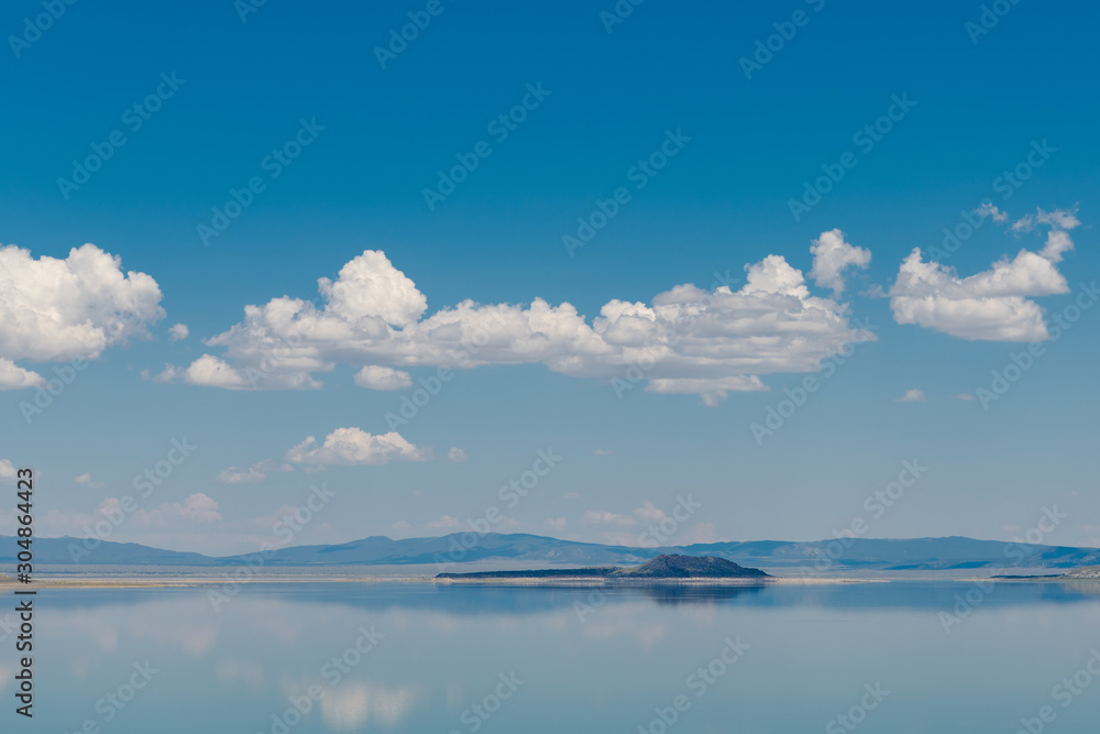 Blue sky with fluffy white clouds reflected in the perfectly still blue waters of Mono Lake, California