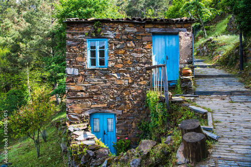 Old rustic stone house with bright blue doors and windows in a lush forest landscape in a village in Portugal