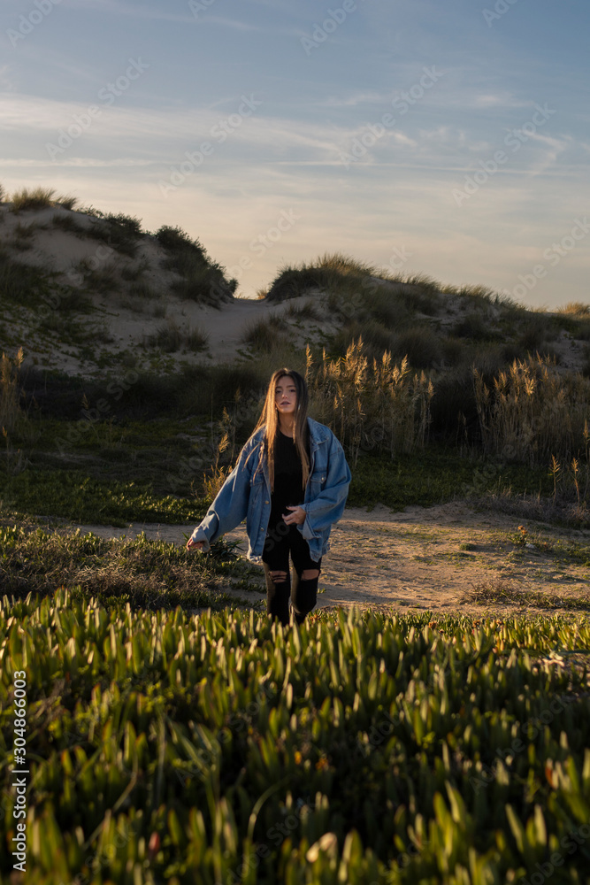 chica joven dirigiéndose a cámara entre dunas y vegetación