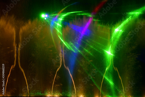 Colorful water fountains. Beautiful laser and fountains show. Large multi colored decorative dancing water jet led light fountain show at night. Dark background. © Uryadnikov Sergey
