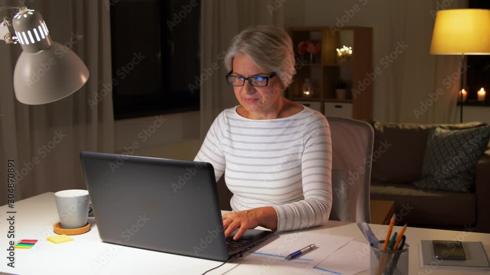 technology, old age and people concept - happy senior woman in glasses with laptop at home in evening technology, old age and people concept - happy senior woman in glasses with laptop at home in evening