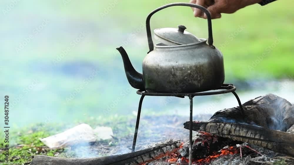 Steaming pot on bonfire background. Smoke above old pot boiling with steam emitted from spout.Small kettle on bonfire campfire at camping trip for make hot drink coffee or tea in morning breakfast . Steaming pot on bonfire background. Smoke above old pot boiling with steam emitted from spout.Small kettle on bonfire campfire at camping trip for make hot drink coffee or tea in morning breakfast .