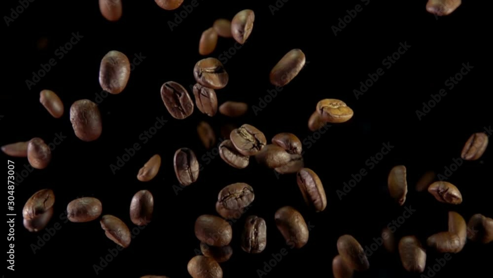 Roasted coffee beans fly up and spin on a black background Roasted coffee beans fly up and spin on a black background