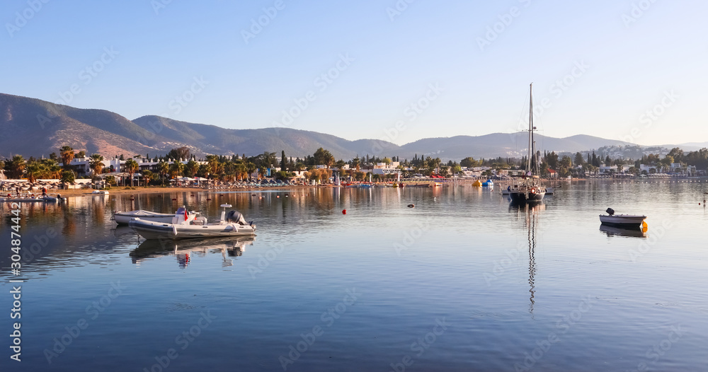 Beautiful bay with calm water, sandy beach, boats and yachts. Small town and green mountains on the coast of the Aegean sea