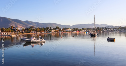 Beautiful bay with calm water, sandy beach, boats and yachts. Small town and green mountains on the coast of the Aegean sea