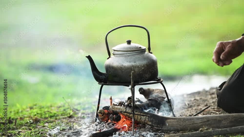 Steaming pot on bonfire background. Smoke above old pot boiling with steam emitted from spout.Small kettle on bonfire campfire at camping trip for make hot drink coffee or tea in morning breakfast . Steaming pot on bonfire background. Smoke above old pot boiling with steam emitted from spout.Small kettle on bonfire campfire at camping trip for make hot drink coffee or tea in morning breakfast .