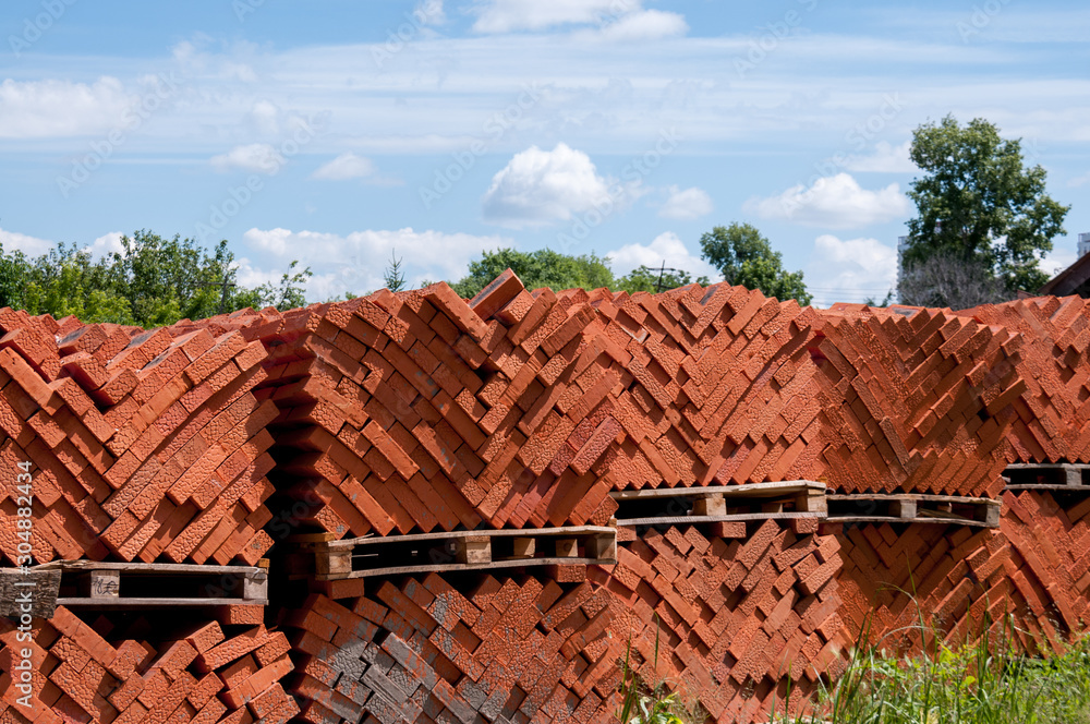 Red bricks stand on pallets on an outdoor construction site in the summer