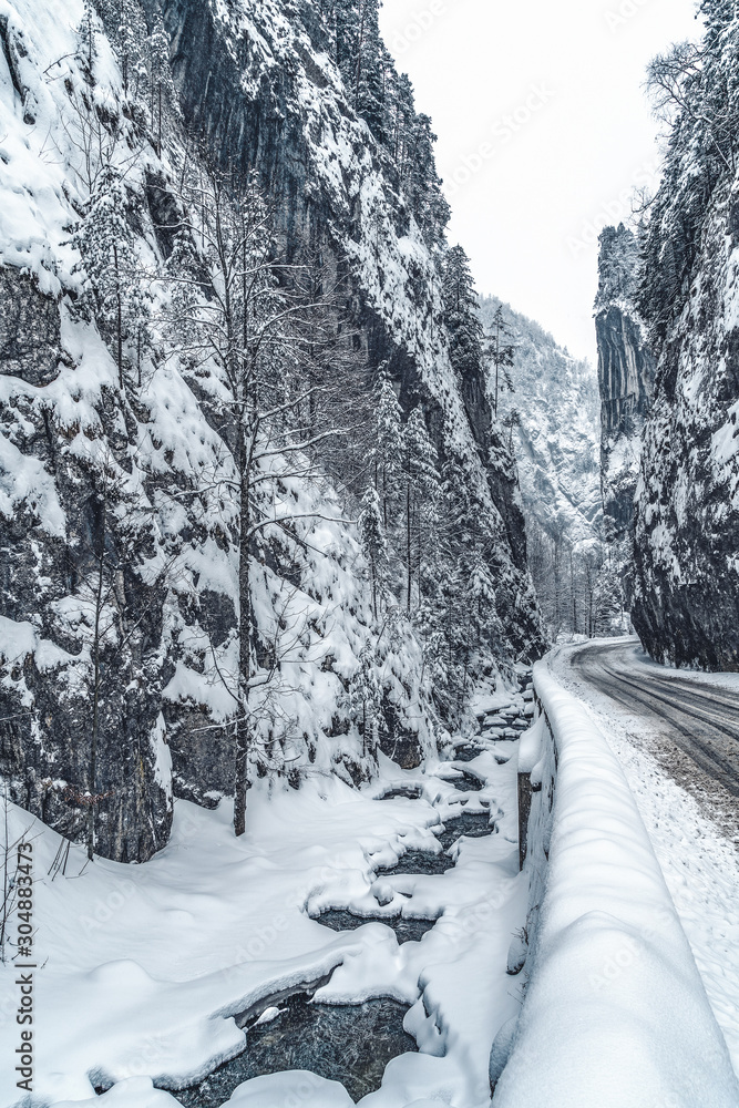 Wintery snowcovered mountain road with white snowy spruces and rocks. Wonderful wintry landscape. Travel background. Transportation