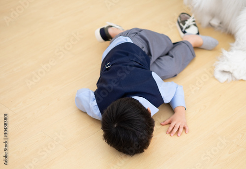An Asia little boy who wear navy suit and bow tie lying on the floor and take off one shoe