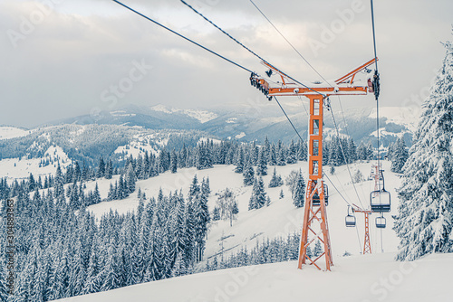 Ski elevator or funicular in snowy forest landscape winter. Panoramic view of frozen mountains background with fir trees covered by snow. Winter holiday and recreation on ski resort