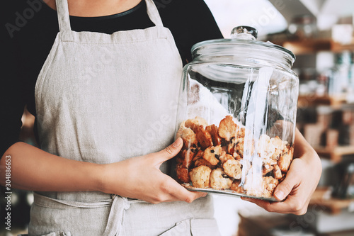 Fotografia Hands hold glass jar with homemade pastry at small local shop.